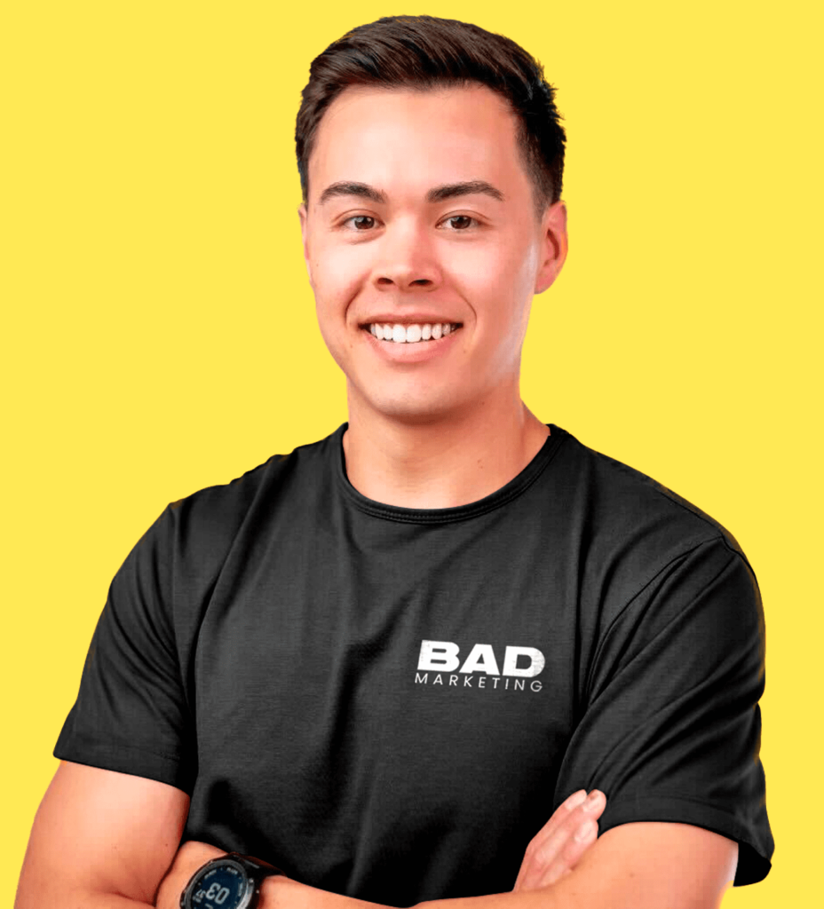 Man in BAD MARKETING t-shirt smiles, arms crossed, at marketing conference 2026 event.