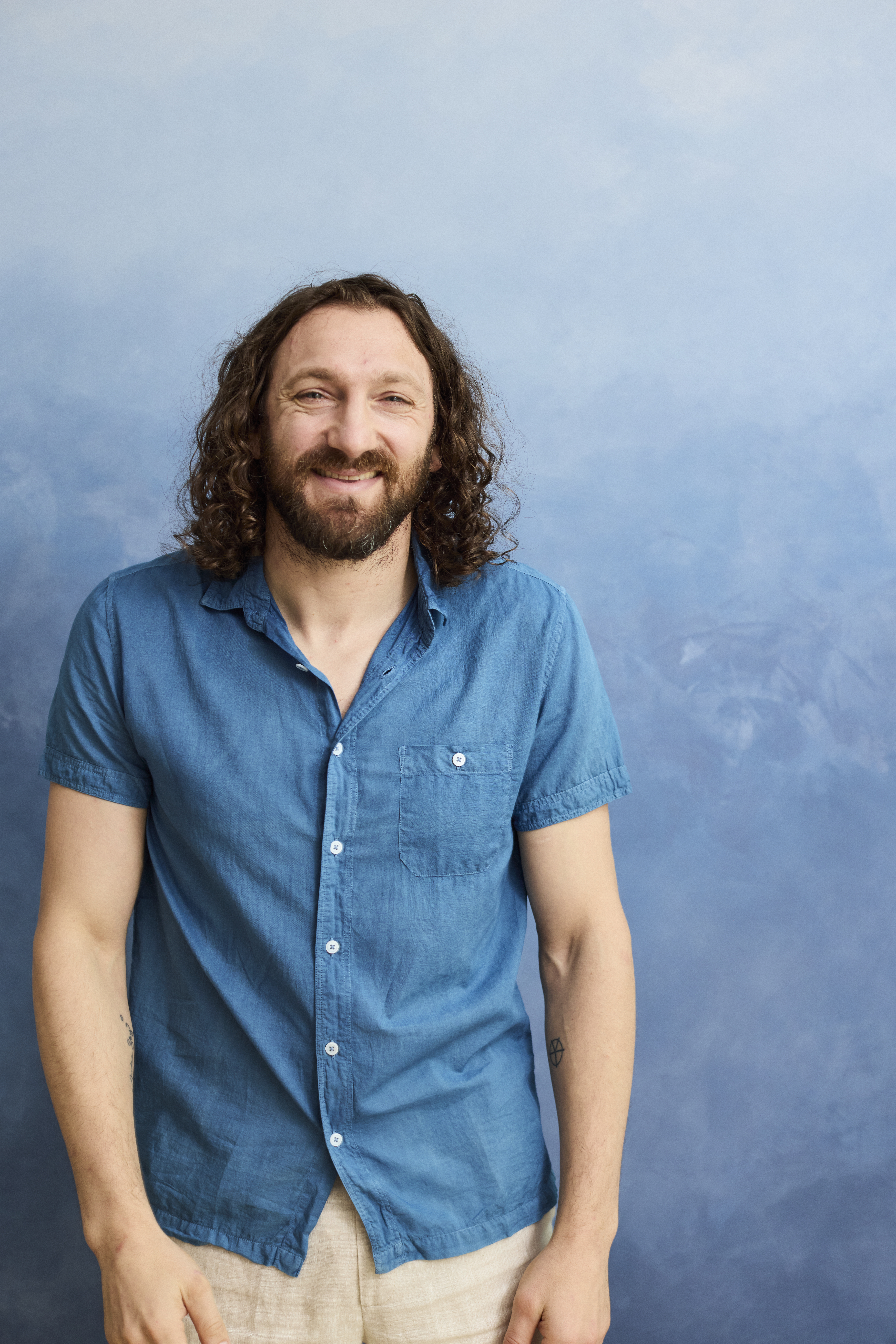 Man with curly hair in blue shirt smiling against blue background